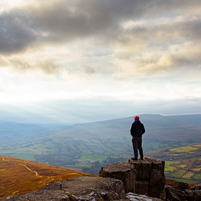 A man standing on a tree stump looking out at the landscape and clouds before him
